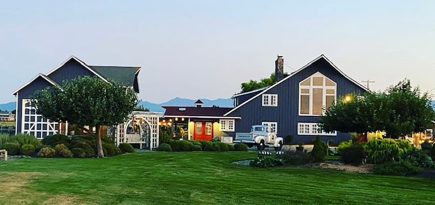Two blue houses with large windows sit beside a lush green lawn, with mountains in the background. Two blue houses with large windows sit beside a lush green lawn, with mountains in the background.