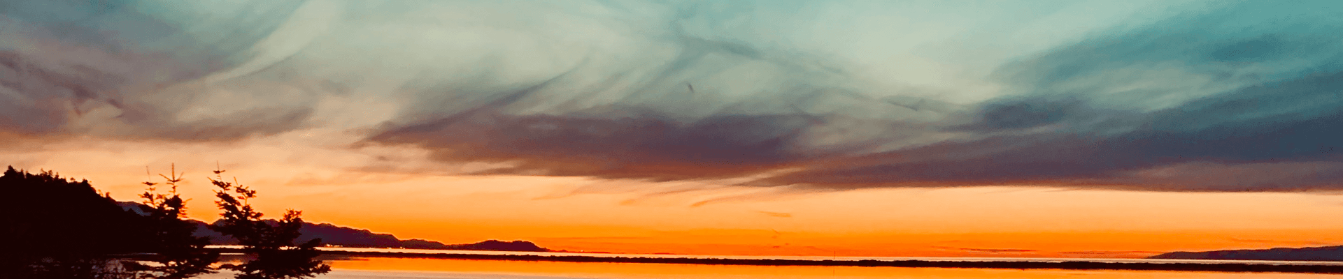 Sunset over a tranquil lake with colorful sky and silhouette of trees.