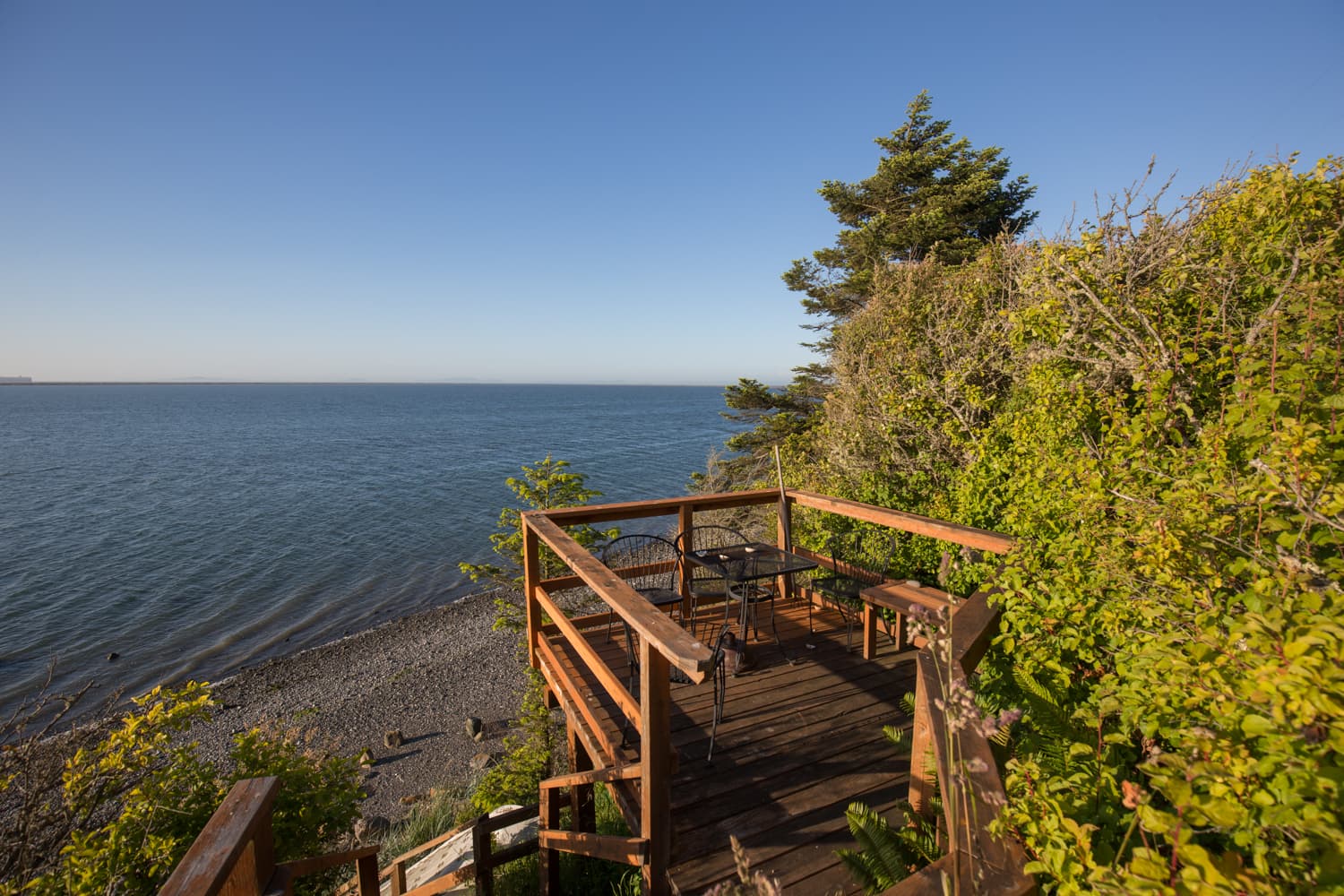 Deck overlooking a calm sea surrounded by greenery under a clear blue sky.