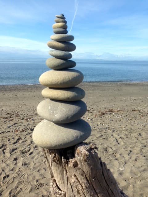 A stack of smooth stones balanced on a driftwood log by the beach.