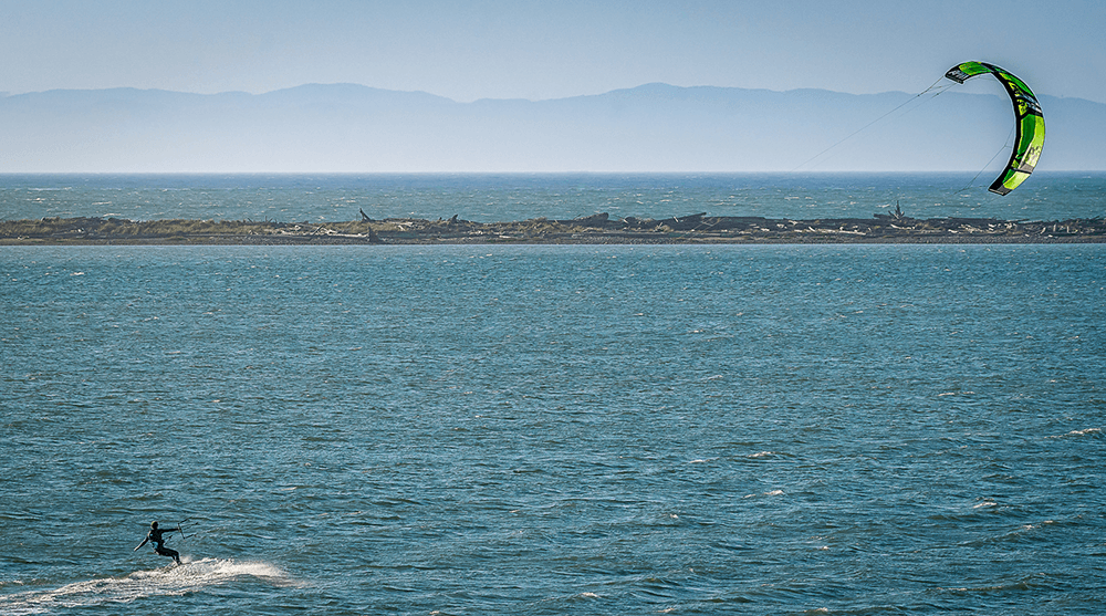 A kitesurfer navigates the ocean with a colorful kite against a backdrop of distant mountains.