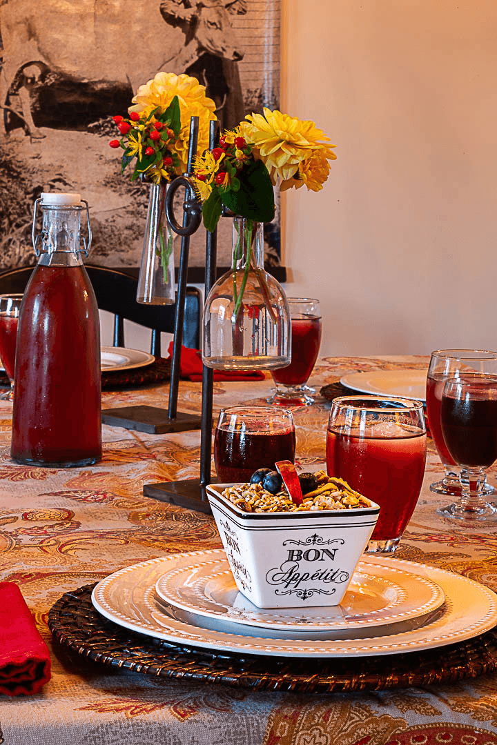 A beautifully set dining table with flowers, drinks, and a bowl of granola.