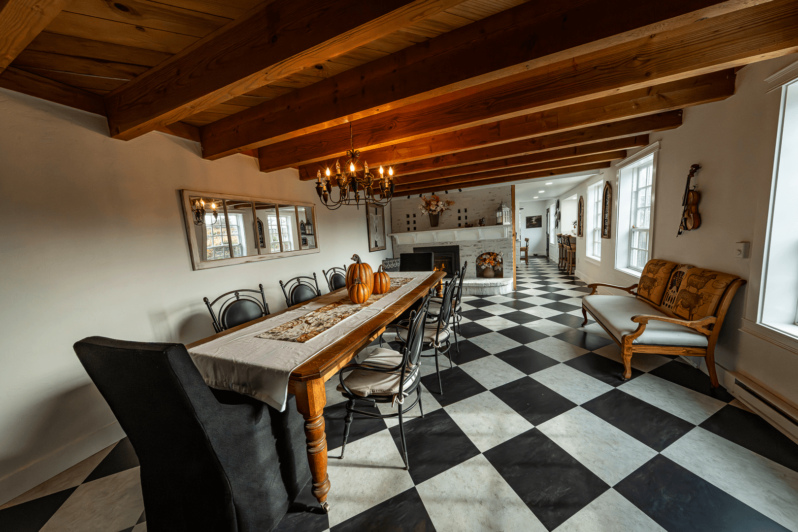 A spacious dining area with a checkered floor, wooden beams, a long table, and a cozy seating arrangement.