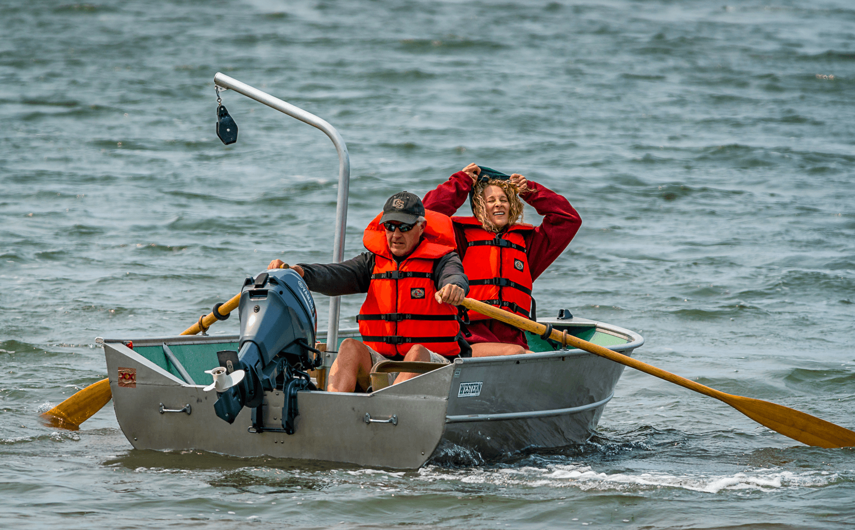 A man and a woman in bright orange life jackets enjoy a lively boat ride on choppy water. The woman smiles, conveying a joyful and adventurous mood.